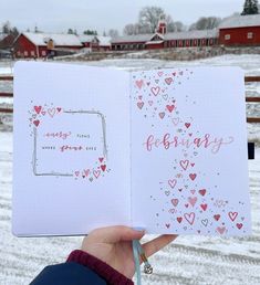 someone holding up a notebook with hearts on it in front of a snow covered field