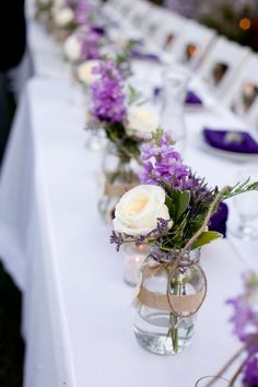 several vases with flowers are lined up on a long table at an outdoor event