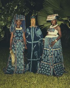 two women dressed in african clothing standing next to each other on the grass with palm trees behind them