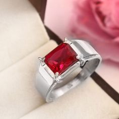 a close up of a ring with a red stone on it and a flower in the background