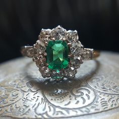 This beautiful vintage emerald and diamond halo ring will melt away your winter blues with its lush green hue! Art Deco Green Diamond Ring Hallmarked, Vintage White Gold Oval Emerald Ring, Vintage Oval White Gold Emerald Ring, Art Deco Green Emerald Ring With Rose Cut Diamonds, Antique Green Oval Diamond Ring, Vintage Oval Emerald Ring In White Gold, Art Deco Emerald Ring With Rose Cut Diamonds, Antique Emerald Diamond Ring For Formal Occasions, Antique Emerald Ring With Brilliant Cut For Formal Occasions