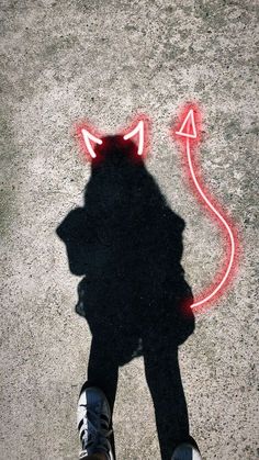 the shadow of a person standing in front of a cat shaped object on concrete with red light coming from it's eyes