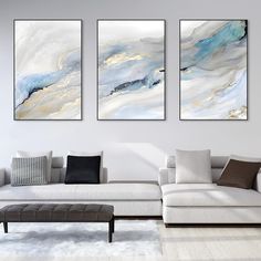 three paintings on the wall above a couch in a room with white furniture and rugs