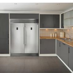 a kitchen with gray and white cabinets, stainless steel refrigerator freezer and wooden counter tops