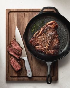 steak in a skillet on a cutting board with a knife and fork next to it