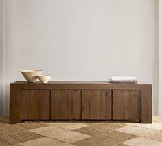 a wooden bench with two bowls on top of it in front of a white wall