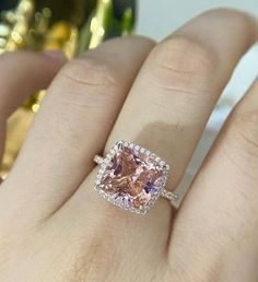 a woman's hand holding an engagement ring with a pink diamond in the center