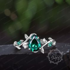 an emerald colored ring with leaves on the sides and green stones in the middle, sitting on top of a black surface