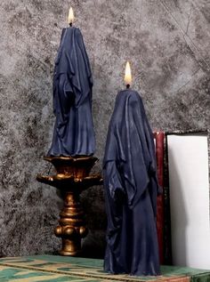 two candles with blue cloth draped over them sitting on a table next to a book