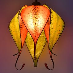 a lamp hanging from the ceiling with an orange and yellow flower on it's side