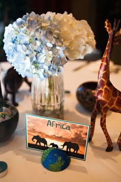 a giraffe figurine sitting on top of a table next to a vase filled with flowers