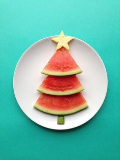 a watermelon christmas tree cut into slices on a white plate with green background