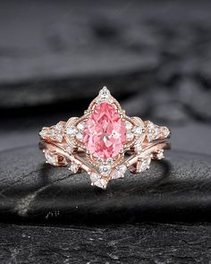 a pink diamond ring sitting on top of a black stone slab with white diamonds around it