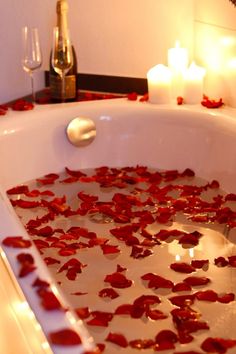 rose petals are floating in a bathtub with candles on the side and wine bottles next to it