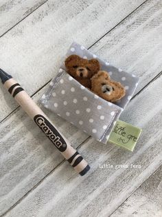 a crayon pencil and two teddy bears in a small box on a wooden table