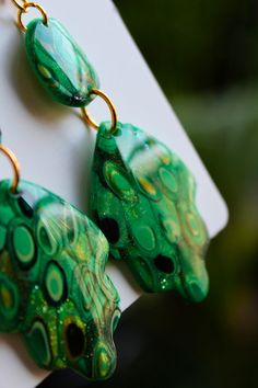 Introducing our "Ireland" collection, a captivating array of handmade polymer clay earrings that are as unique as they are stunning. Each pair is meticulously crafted to embody the lush landscapes and rich heritage of Ireland, featuring deep green hues accented with elegant touches of gold.  Available in two exquisite color editions, these earrings are not only a testament to craftsmanship but also a piece of art that you can wear.  Their hard and shiny finish not only adds to their allure but a Artistic Green Earrings For Gift, Green Hand-painted Polymer Clay Earrings, Hand Painted Green Earrings In Polymer Clay, Hand Painted Green Polymer Clay Earrings, Green Resin Drop Earrings, Green Hand Painted Polymer Clay Earrings, Artistic Green Drop Earrings, Green Hand Painted Drop Earrings, Handmade Artistic Green Earrings