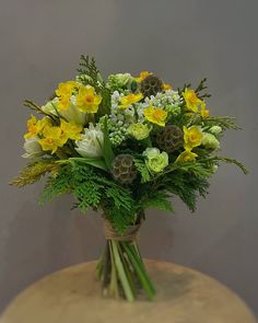 a vase filled with yellow and white flowers on top of a wooden table next to a gray wall