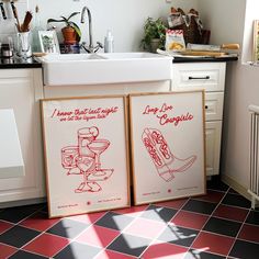 two framed posters sitting on top of a kitchen floor next to a sink and stove