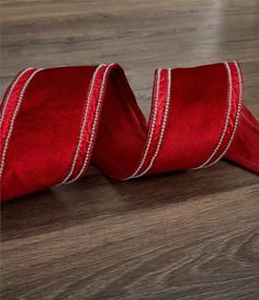 a red satin ribbon on a wooden floor with white thread and bead trim around the edge