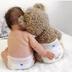 a baby in diapers is hugging a teddy bear