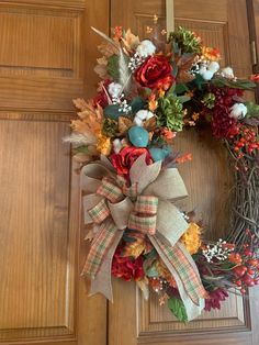 a wreath on the front door with flowers and leaves hanging from it's side