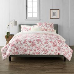 a bed in a room with white walls and wood flooring is covered by a red floral comforter