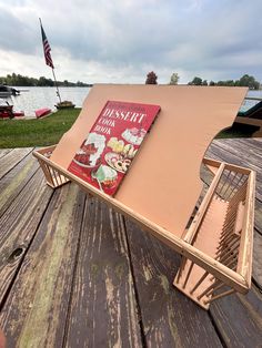 an upside down book is sitting on a wooden table next to the water with boats in the background