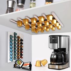 there is a coffee maker and some cups on the shelf in this kitchen with gold lids