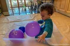 a young child playing with balloons in a plastic container on the floor near a table