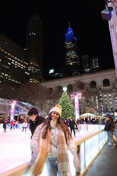 people skating on an ice rink at night in front of a christmas tree and skyscrapers