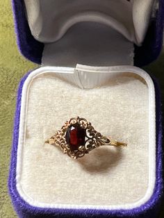 an antique ring with a red stone sits in a purple box on the floor next to a pair of white shoes