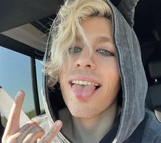 a young man sticking his tongue out in the back seat of a car while wearing a hoodie