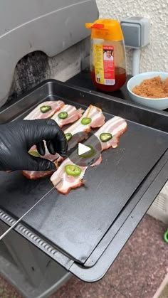 a person in black gloves cooking food on top of an outdoor grill with other ingredients