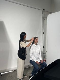 a woman is getting her hair styled by another woman in front of a white wall