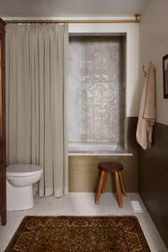 a bath room with a toilet a rug and a shower curtain next to a tub