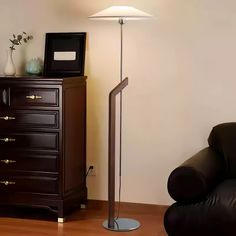 a living room with a black chair and a lamp on top of a dresser next to a white wall