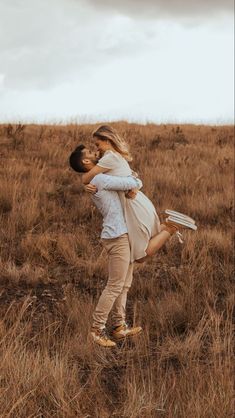 a man and woman are hugging in the middle of a field with tall brown grass