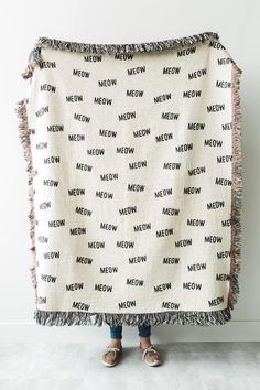 a person standing in front of a white wall holding a blanket with the words meow printed on it