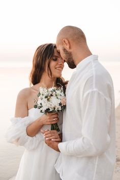 a man and woman standing next to each other near the ocean with flowers in their hands