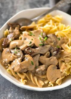 a white bowl filled with pasta and meat covered in mushroom gravy next to a fork