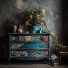 a blue dresser with flowers and vases sitting on it's top, against a dark background