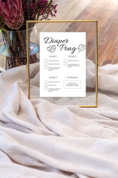 a diaper pong sign sitting on top of a bed next to a vase filled with flowers