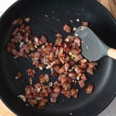 bacon being cooked in a skillet with a wooden spoon