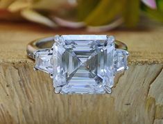 an emerald - cut diamond ring with three baguets sits on a piece of wood