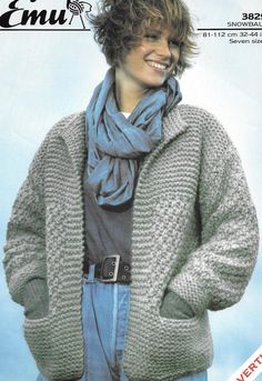 a woman wearing a gray sweater and blue jeans with a scarf around her neck is smiling