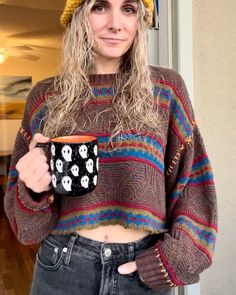 a woman wearing a hat and sweater holding a coffee cup