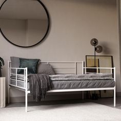 a white metal day bed in a room with a round mirror on the wall above it