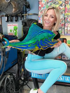 a woman is holding a large fish in her hands and smiling at the camera while sitting on a stool