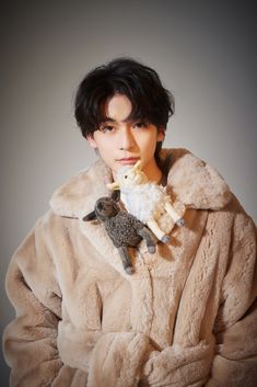 a young man in a fur coat holding two sheeps on his shoulder and looking at the camera