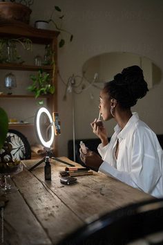 a woman sitting at a table in front of a mirror with a light on it